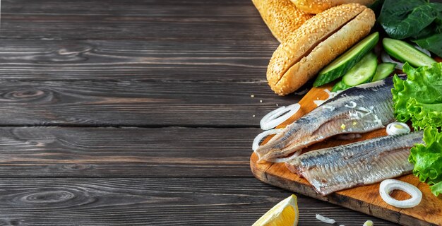 Making herring fillet sandwich with onions, cucumber and salad on a wooden board