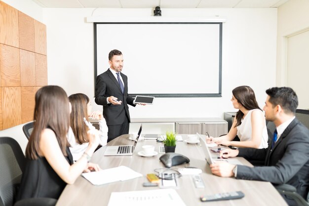 Male accountant holding digital tablet while planning budget with team in boardroom