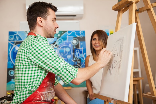 Free photo male artist drawing a sketch of a beautiful young woman in his studio