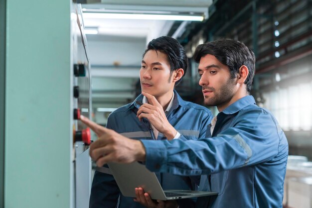 Male Asian caucasian engineer professional having a discussion standing consult at machine in the factory two expert coworker brainstorm explaining and solves the process of the cnc operate machine