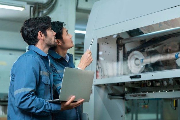 Free photo male asian caucasian engineer professional having a discussion standing consult at machine in the factory two expert coworker brainstorm explaining and solves the process of the cnc operate machine