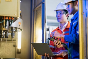 Male asian engineer professional having a discussion standing concult cnc machine in the factory two asian coworker brainstorm explaining and solves the process of the cnc operate machine