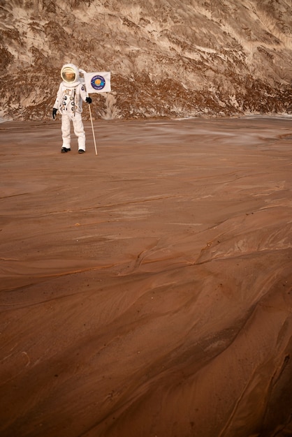 Male astronaut holding a flag stuck in soil on an unknown planet