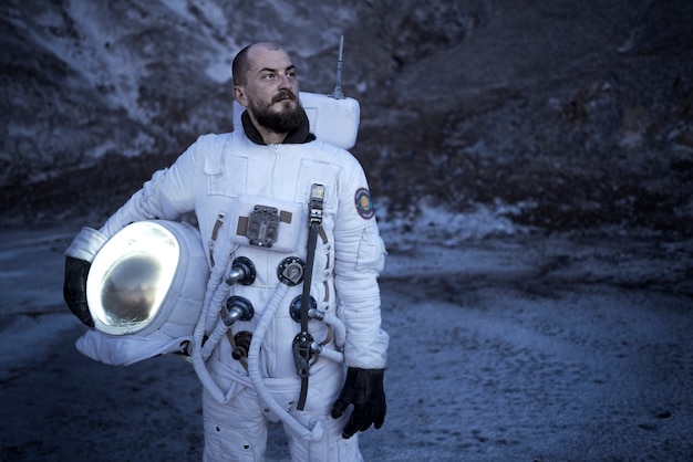 Мужчина-космонавт держит шлем и осматривается во время космической миссии на неизвестной планете