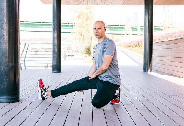 Male athlete doing stretching exercise wearing bluetooth on his ear