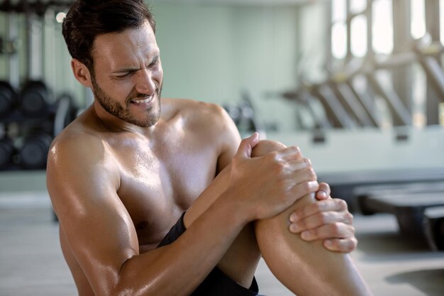 체육관에서 운동하는 동안 고통에 그의 무릎을 잡고 남자 운동 선수