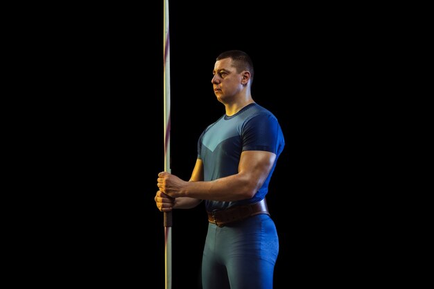 Спортсмен-мужчина тренируется в метании копья на черном в неоновом свете.