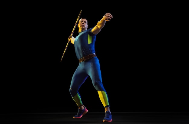 Free photo male athlete practicing in throwing javelin isolated on black studio in neon light