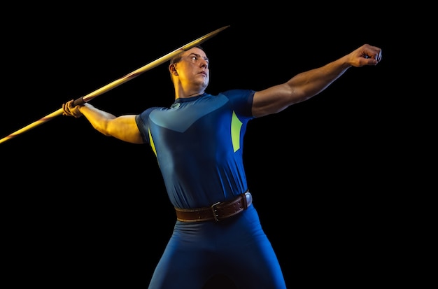 Male athlete practicing in throwing javelin isolated on black studio in neon light