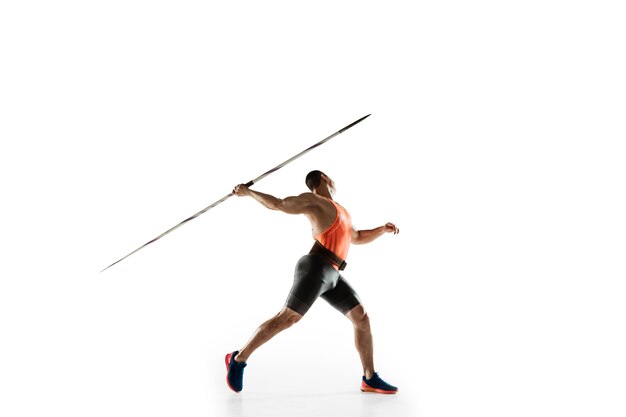 Male athlete practicing in throwing javelin on white studio.