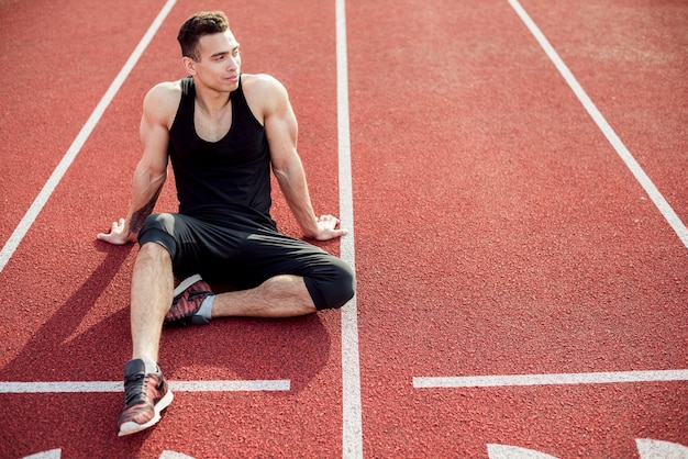 Male athlete relaxing on red race track
