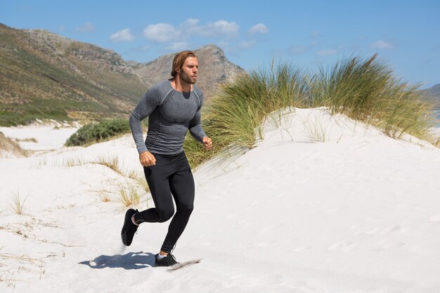 Male athlete running at beach by mountain