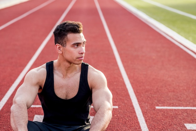 Foto gratuita un atleta di sesso maschile seduto sulla pista da corsa guardando lontano