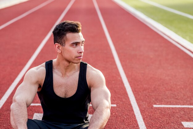 A male athlete sitting on race track looking away