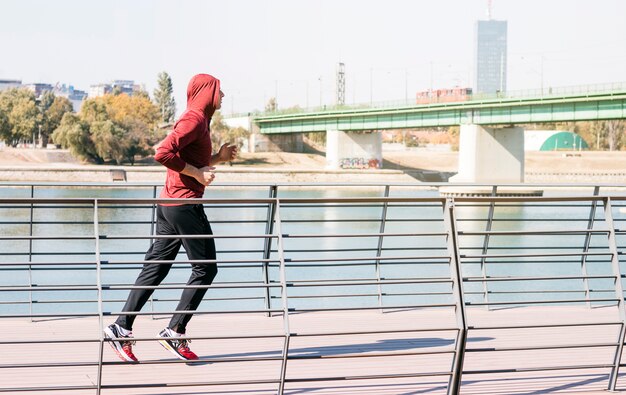 Male athlete wearing sweatshirt hoodie running near the lake