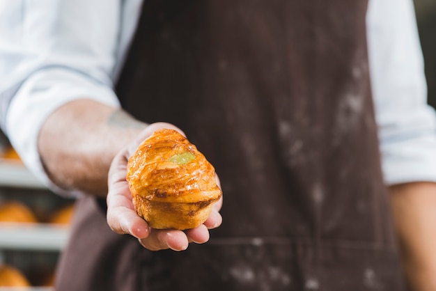 焼きたての甘いパフペストリーを保持しているエプロンの男性ベイカー