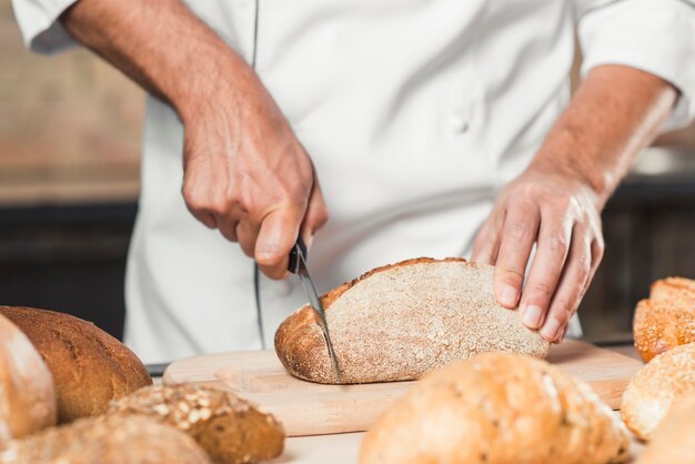 Male baker cutting loaf of bread on chopping bread