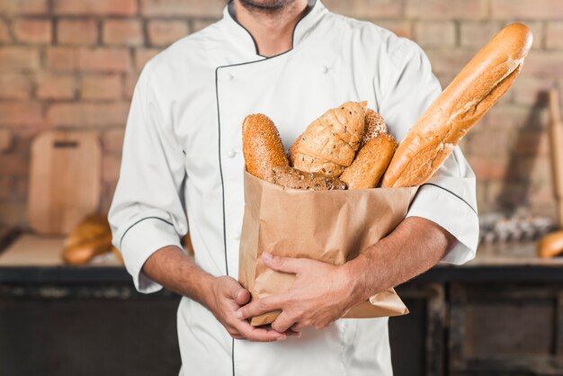 Male baker holding paper bag with different loaf of breads