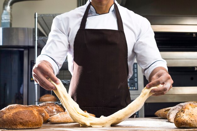 Foto gratuita panettiere maschio impastando la pasta sul tavolo di legno