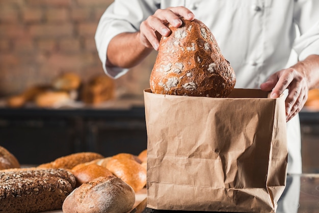 Male baker putting baked bread in brown paper bag