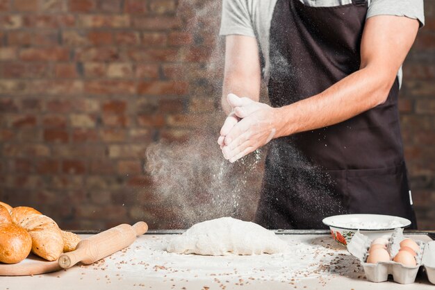 Мужская пекарьская рука, пылящая муку, на замешанном тесто на кухонной столешнице