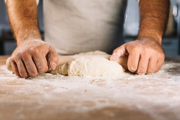 Male baker's hand flattening dough with rolling pin