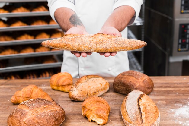 A male baker's hand holding baguette bread over the table in the commercial kitchen
