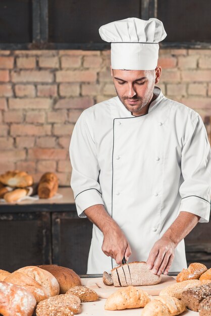 Male baker in uniform cutting bread slice on table