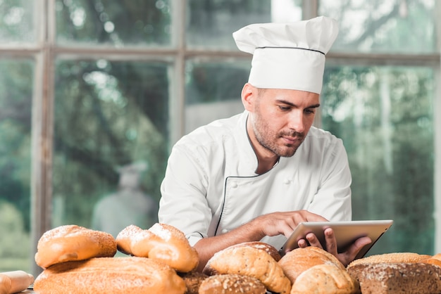 Male baker using digital tablet with many breads on table