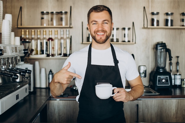 カウンターでカップを保持しているコーヒーショップで男性のバリスタ