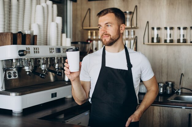 段ボールのカップにコーヒーを保持している男性のバリスタ