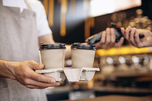 Male barista holding terminal while customer paying with card