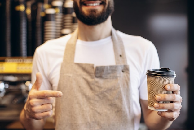 板紙のカップでコーヒーを提供する男性のバリスタ