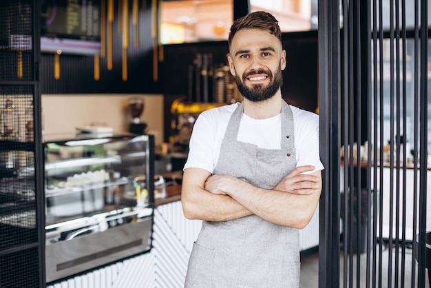 Foto gratuita barista maschio in piedi e sorridente in una caffetteria