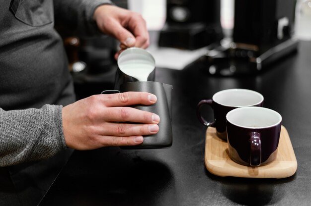 Male barista with apron pouring frothed milk for coffee cups