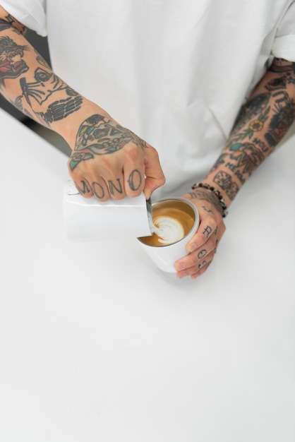 Male barista with tattoos adding milk to coffee