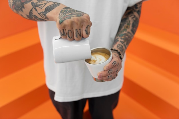 Male barista with tattoos adding milk to coffee