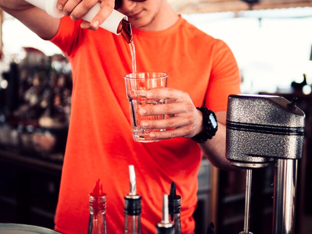 Male bartender filling glass with clear drink 