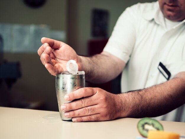 Male bartender filling shaker with ice cubes