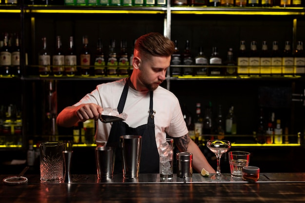 Мужчина-бармен делает коктейль с шейкером