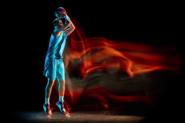 Баскетболист мужского пола, играющий в баскетбол, изолированный над темной стеной студии в смешанном свете.