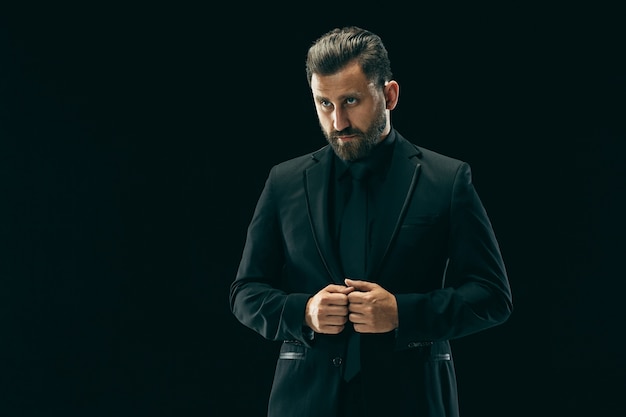 Male beauty concept. Portrait of a fashionable young man with stylish haircut wearing trendy suit posing over black background.