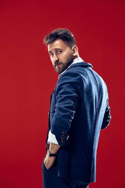 Free photo male beauty concept. portrait of a fashionable young man with stylish haircut wearing trendy suit posing over red.