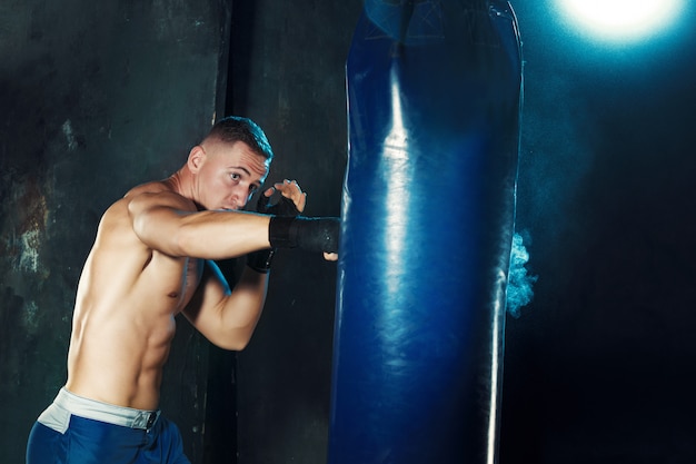 Male boxer boxing in punching bag with dramatic edgy lighting