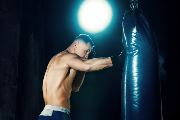 Male boxer boxing in punching bag with dramatic edgy lighting