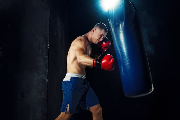 Foto gratuita boxer maschio nel sacco da boxe con drammatica illuminazione tagliente