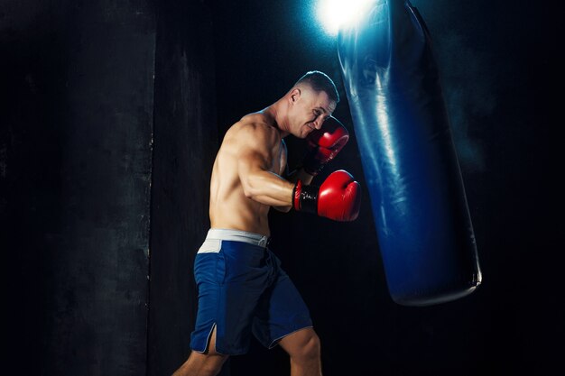 Male boxer boxing in punching bag with dramatic edgy lighting