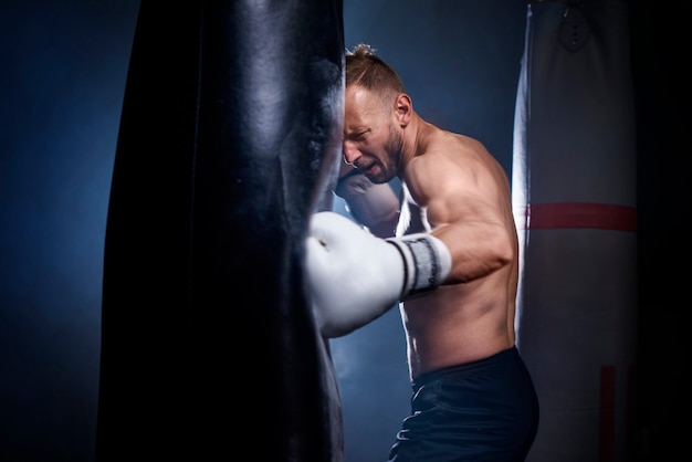 Foto gratuita pugile maschio che usa il sacco da boxe durante l'allenamento