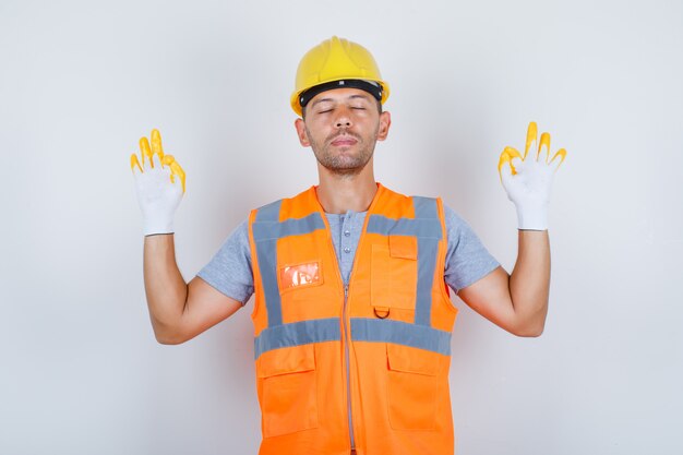 Male builder doing meditation with closed eyes in uniform, front view.