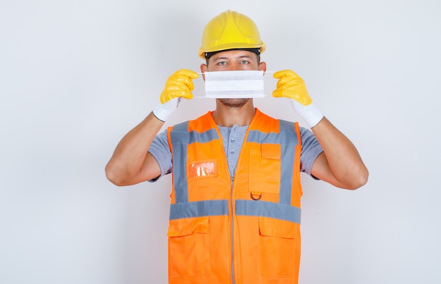 Free photo male builder holding medical mask over face in uniform, helmet, gloves, front view.
